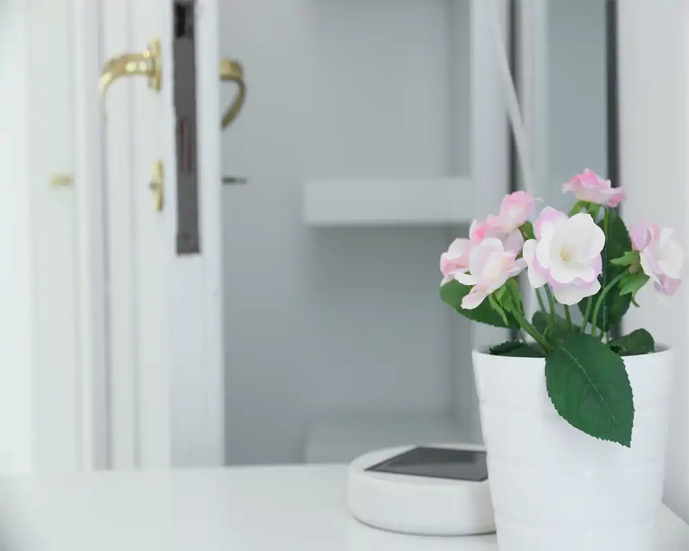Vignetta d'ingresso minimal e luminosa con un tavolino bianco, un vaso di fiori decorativo e una porta parzialmente aperta con maniglia dorata; atmosfera pulita e accogliente.