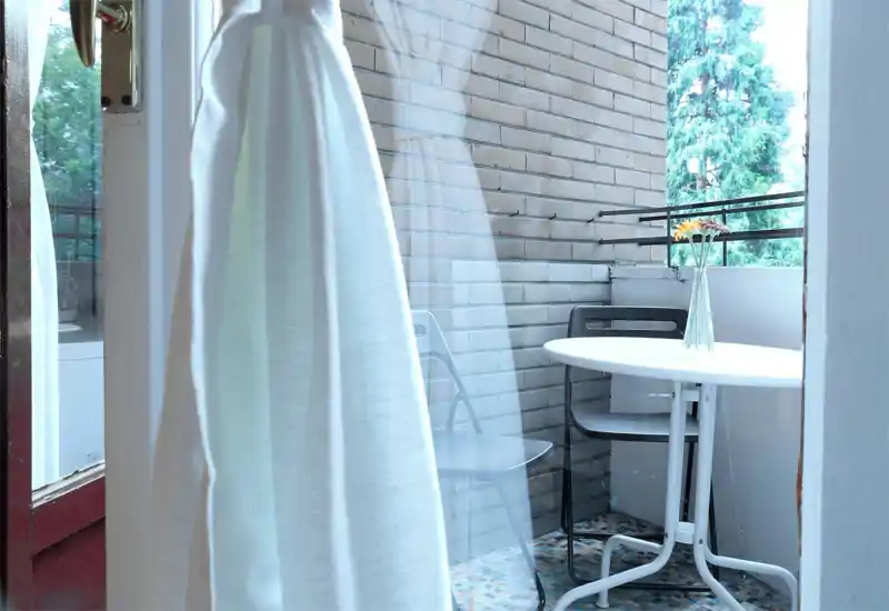 Pequeño balcón privado con mesa blanca redonda, dos sillas y un jarrón con flores. Rincón exterior agradable, ideal para el café de la mañana.