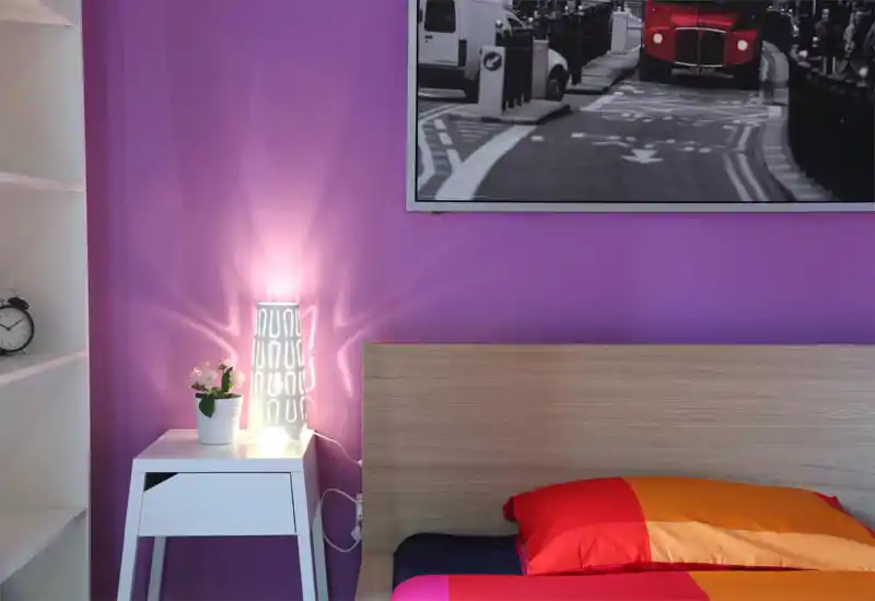 Rincón de dormitorio luminoso y colorido con cabecero de madera, ropa de cama roja-naranja intensa y mesita con lámpara decorativa y planta — perfecto para fotos acogedoras del anuncio.