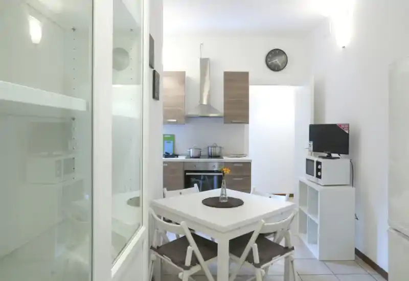 Bright, modern open kitchen with wooden cabinets, stainless-steel hood and a small dining table for four. Clean, tidy space ideal for short-term rentals or compact apartments.