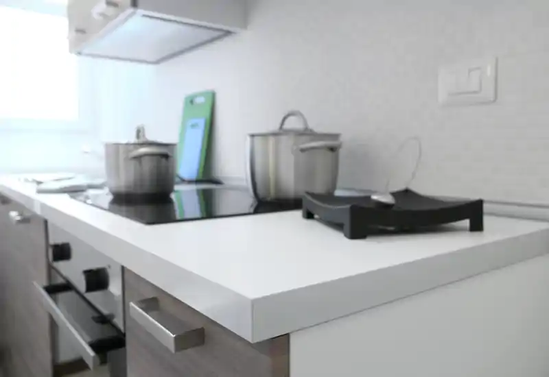 Bright modern kitchen countertop with induction hob, stainless pots and a clean white work surface; minimalist and functional styling ideal for rental photos.