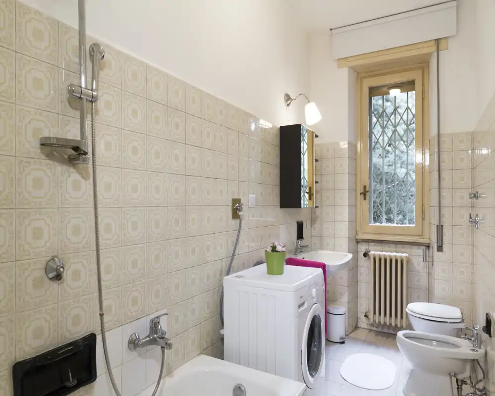 Bagno luminoso e ben curato con vasca, doccia, lavabo, wc e bidet; presente una lavatrice e una finestra alta che garantisce luce naturale.