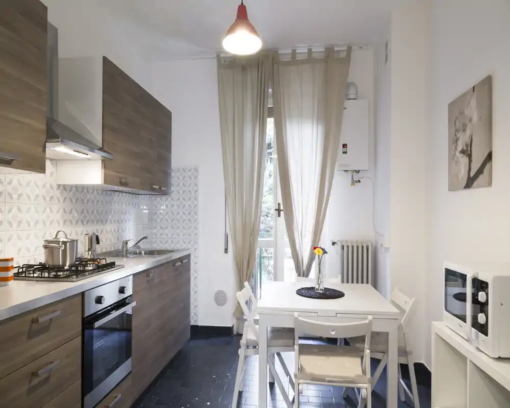 Cucina moderna e luminosa con pensili effetto legno, piano cottura a gas e piccolo tavolo da pranzo vicino alla finestra — accogliente e ben organizzata per affitti brevi.