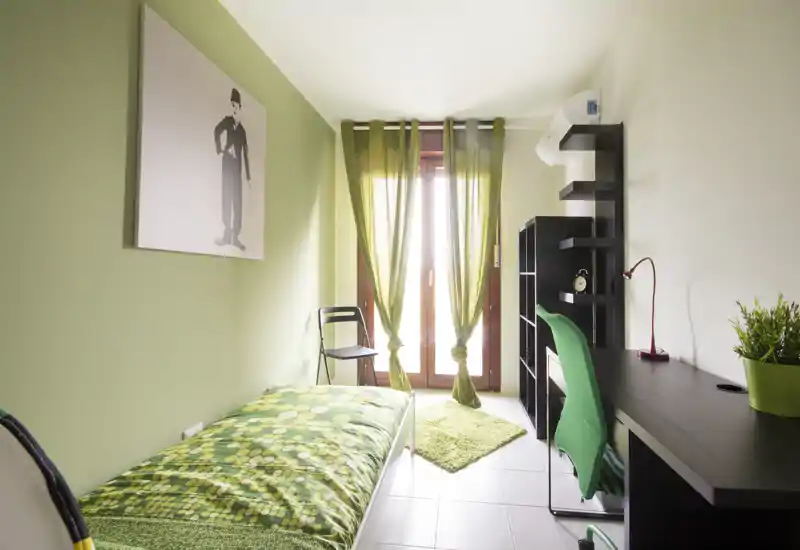 Bright, single bedroom with coordinated green décor, a desk and shelving — ideal for a student or single occupant. Natural light from the balcony door and a compact layout make the room practical and welcoming.