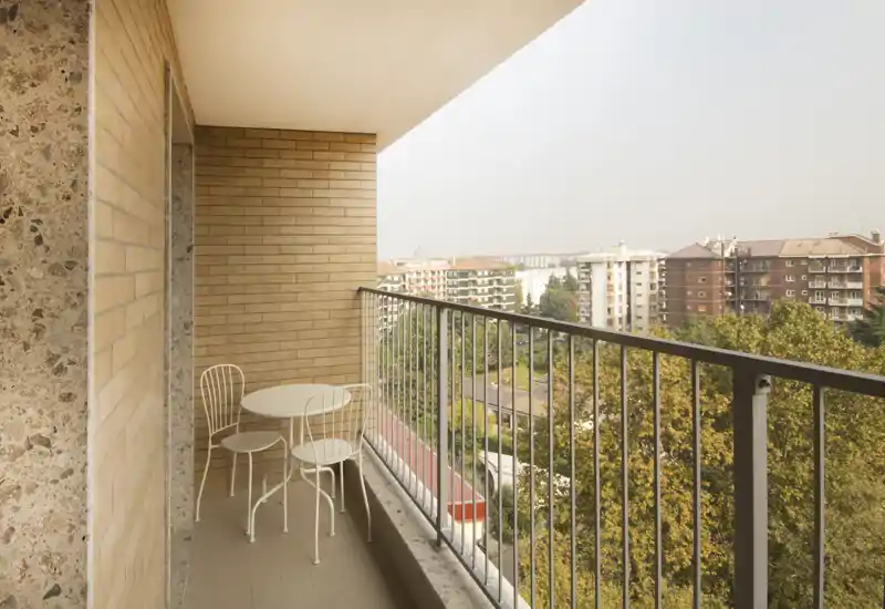 Sunny balcony with a small round table and two chairs overlooking tree-lined residential buildings — ideal for morning coffee or relaxing outdoors.