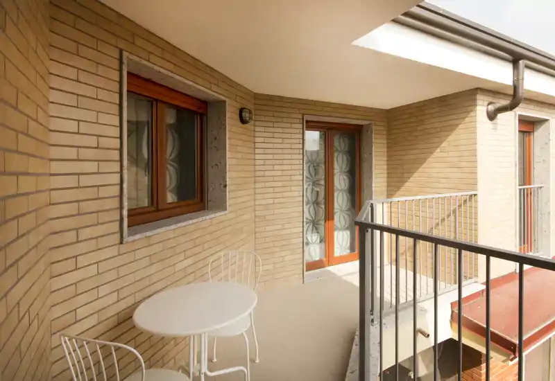 Sunny covered balcony with brick walls, metal railing and a small round table with chairs — a cozy spot for morning coffee.