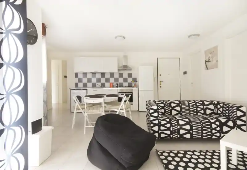 Bright, modern living area with a patterned black-and-white sofa, small dining table and open kitchenette — ideal for a compact apartment.