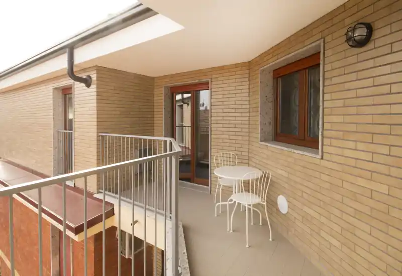 Sunny covered balcony with a small round bistro table and two chairs, brick walls and metal railing—ideal for morning coffee.