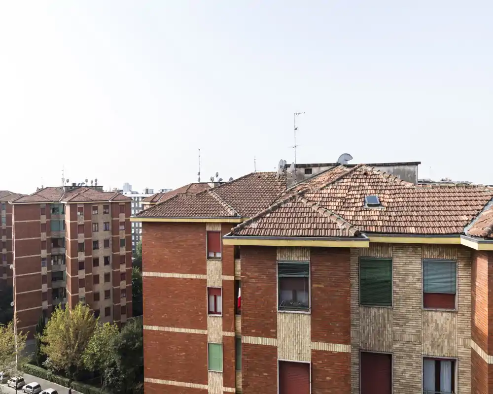 Vista exterior urbana con edificios vecinos y tejados de teja bajo un cielo despejado.