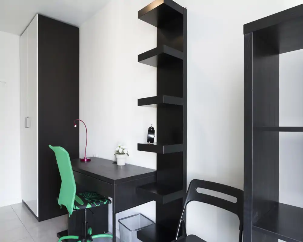 Rincón de trabajo luminoso y minimalista con escritorio oscuro, estanterías y una silla verde — ordenado y moderno, ideal para estudio o teletrabajo.