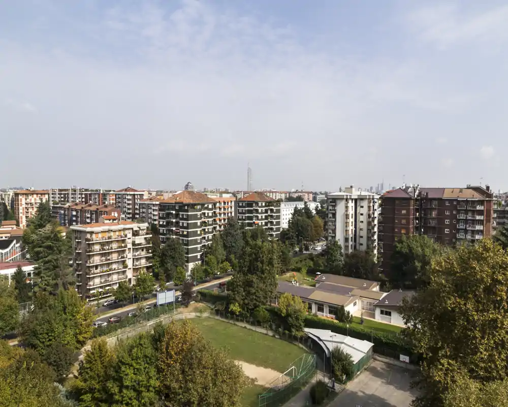 Wide outdoor city view from a high floor showing residential buildings, trees and a small sports field; bright daylight and good visibility.