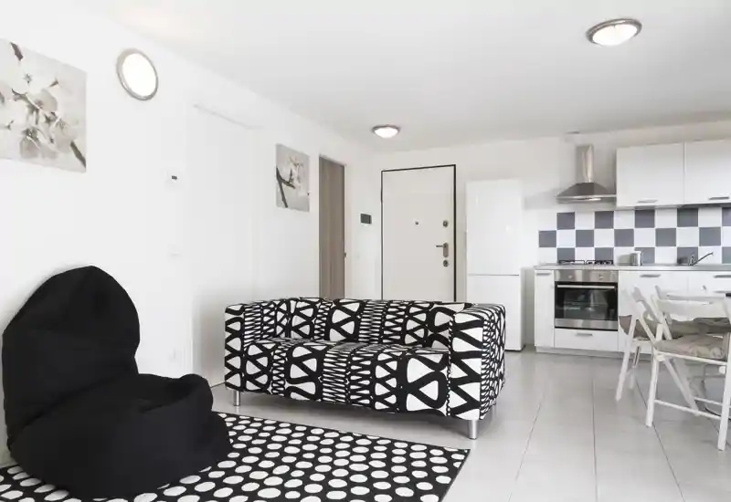 Modern open-plan living area with a patterned black-and-white sofa, beanbag chair and an integrated kitchen. Bright, minimalist styling and coordinated textiles make this space feel contemporary and welcoming.