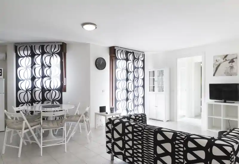 Bright, modern living area with bold black-and-white patterned sofa, a small dining nook and clean minimalist furnishings.