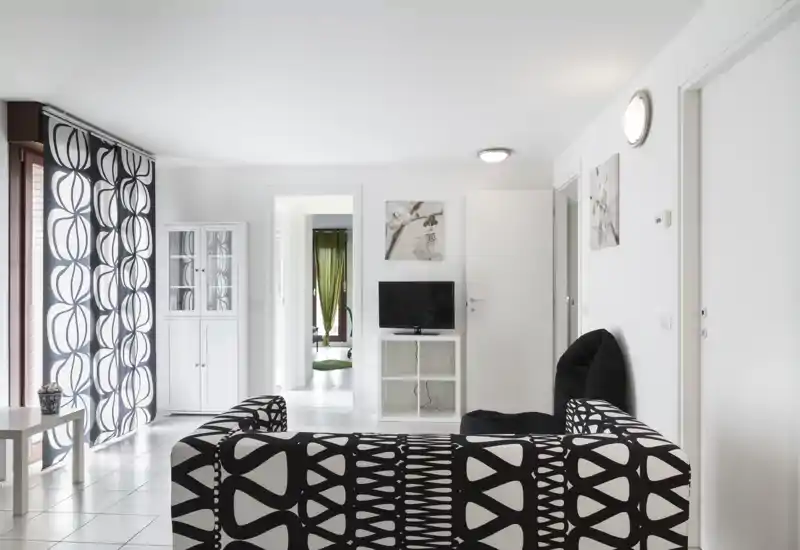 Bright, modern living room with a bold patterned sofa, matching curtains and a compact TV unit—clean white walls and tiled floor create an airy, minimalist space.