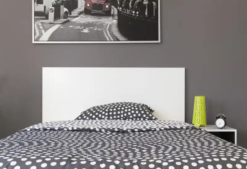 Camera da letto moderna e luminosa con letto matrimoniale al centro, biancheria a pois, comodino con lampada e sveglia; testiera minimal e quadro appeso completano l'arredo.