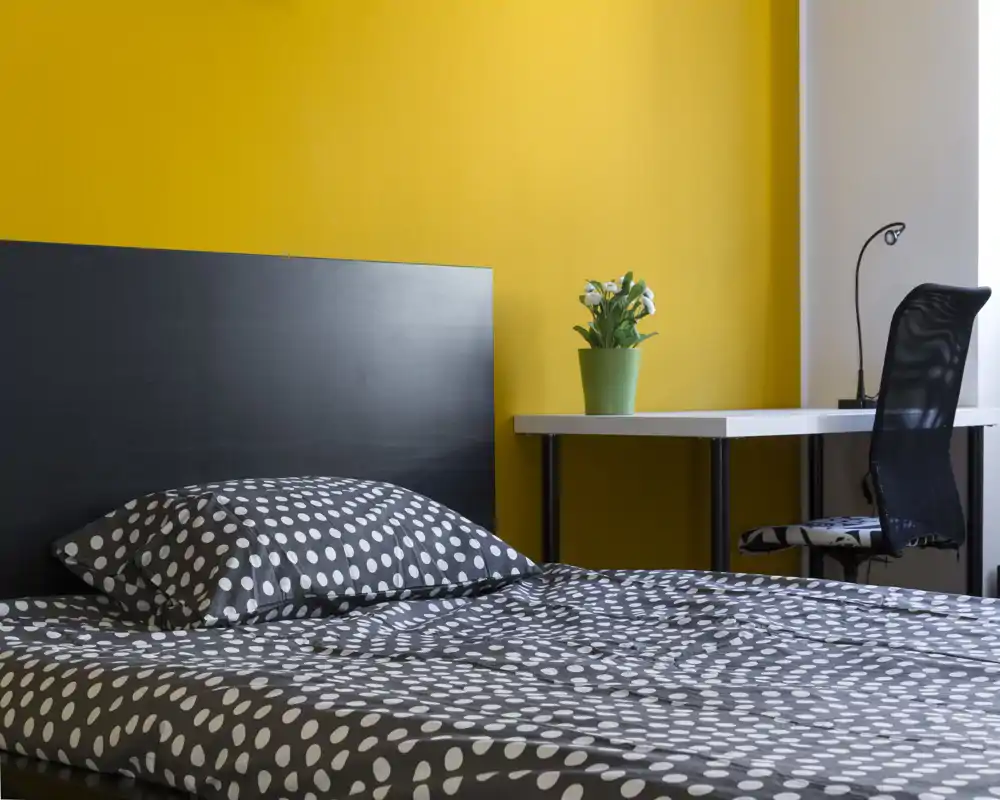 Camera da letto moderna e luminosa con copriletto a pois, testiera nera e una scrivania vicino alla finestra — ideale per affitti brevi.