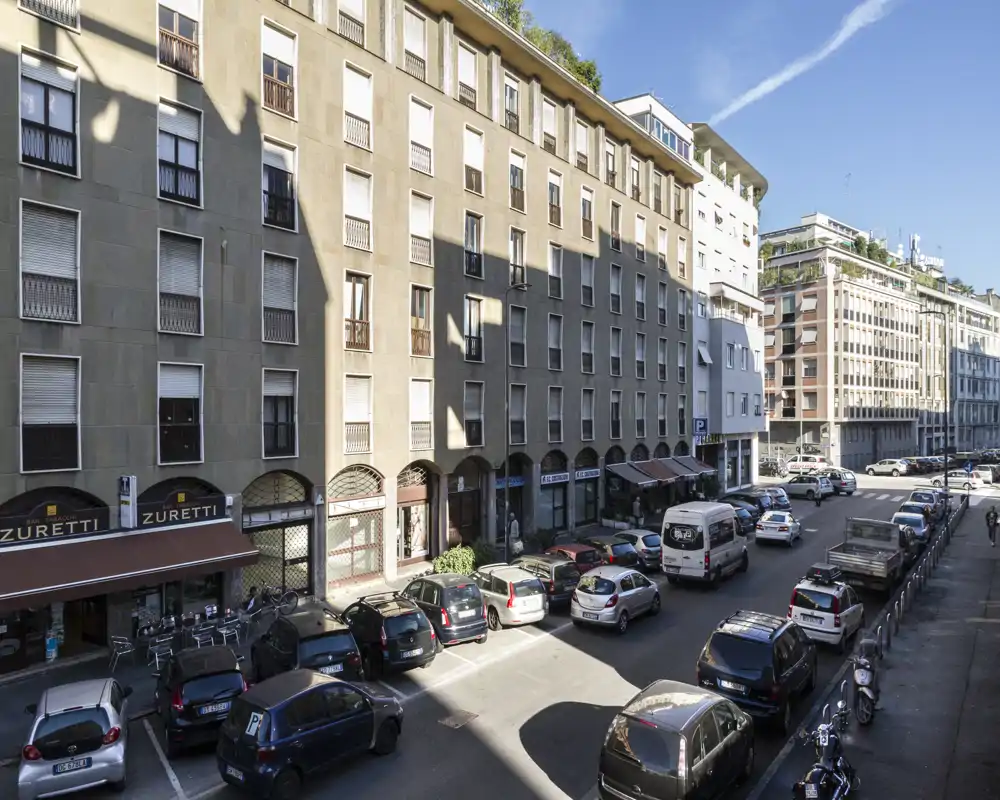 Rue urbaine ensoleillée avec voitures garées, immeubles bas et commerces en rez-de-chaussée ; vue nette idéale pour présenter l'emplacement et la façade sur rue.