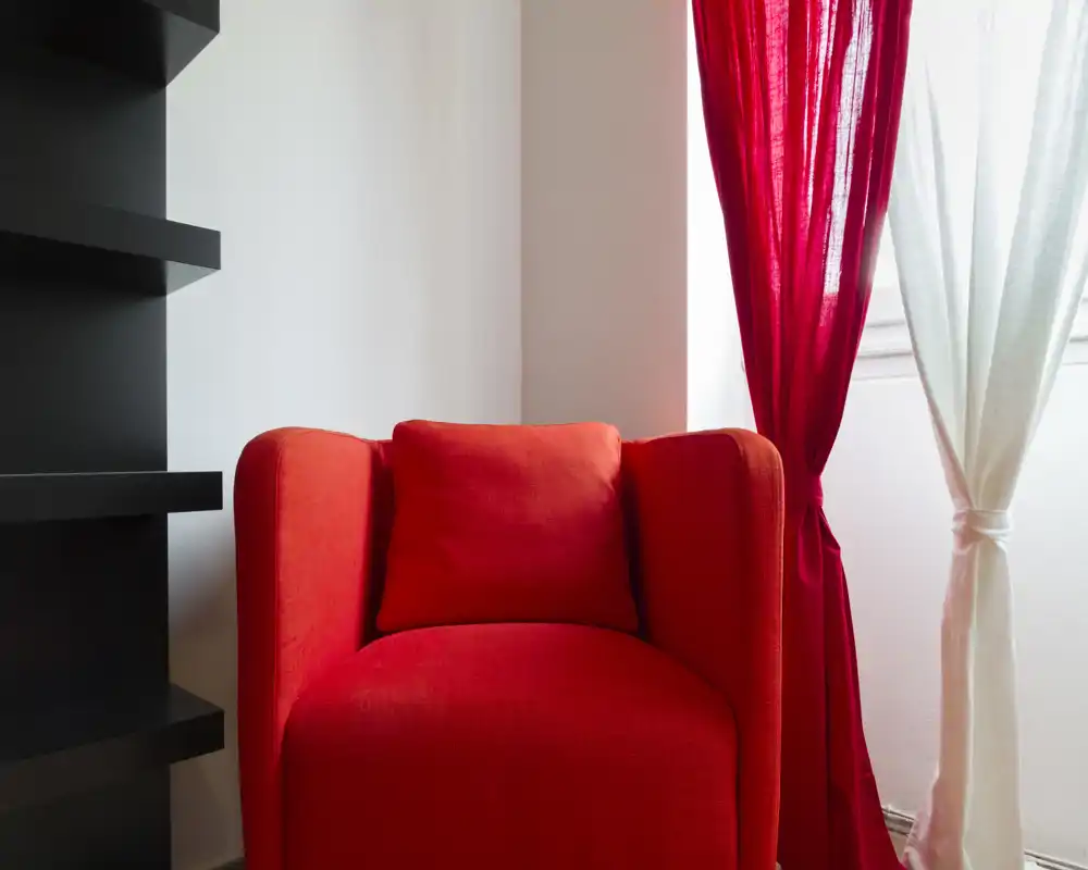 Angolo living luminoso e moderno con una poltrona rossa accesa, tenda coordinata e luce naturale morbida dalla finestra.