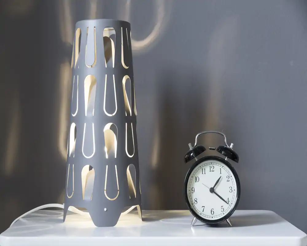 Close-up of a bedside surface with a decorative table lamp and a classic twin-bell alarm clock, ideal for highlighting bedroom accessories and lighting in a listing.