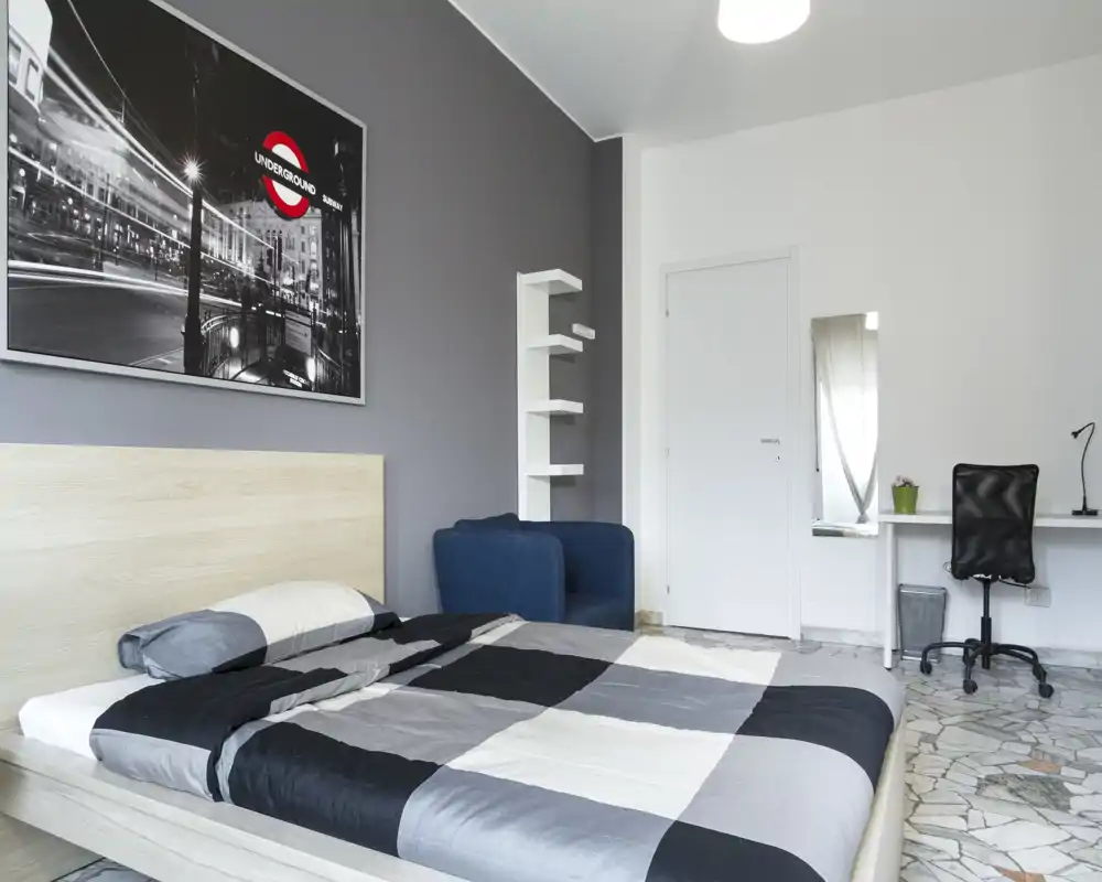 Bright, modern bedroom with a large bed, patterned bedding, a comfortable blue armchair and a small desk — clean, minimal and well-lit for rental photos.