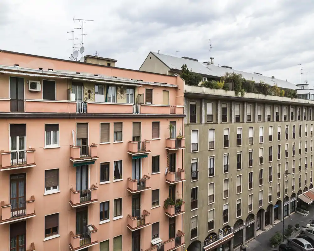 Street-level exterior view of neighboring apartment buildings with balconies and a small rooftop garden; good for showcasing the building façade and urban context.