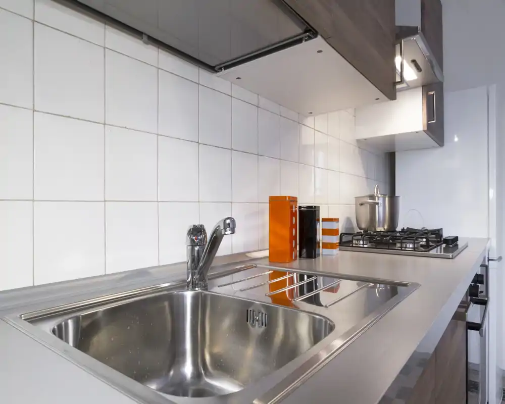 Modern compact kitchen with a stainless-steel sink, faucet and built-in gas hob; white tiled backsplash and minimal countertop accessories create a clean, functional look.