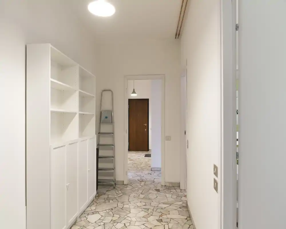 Bright, clean entrance hallway with built-in shelving, stone-patterned floor and overhead lighting — a neat transitional space into the apartment.