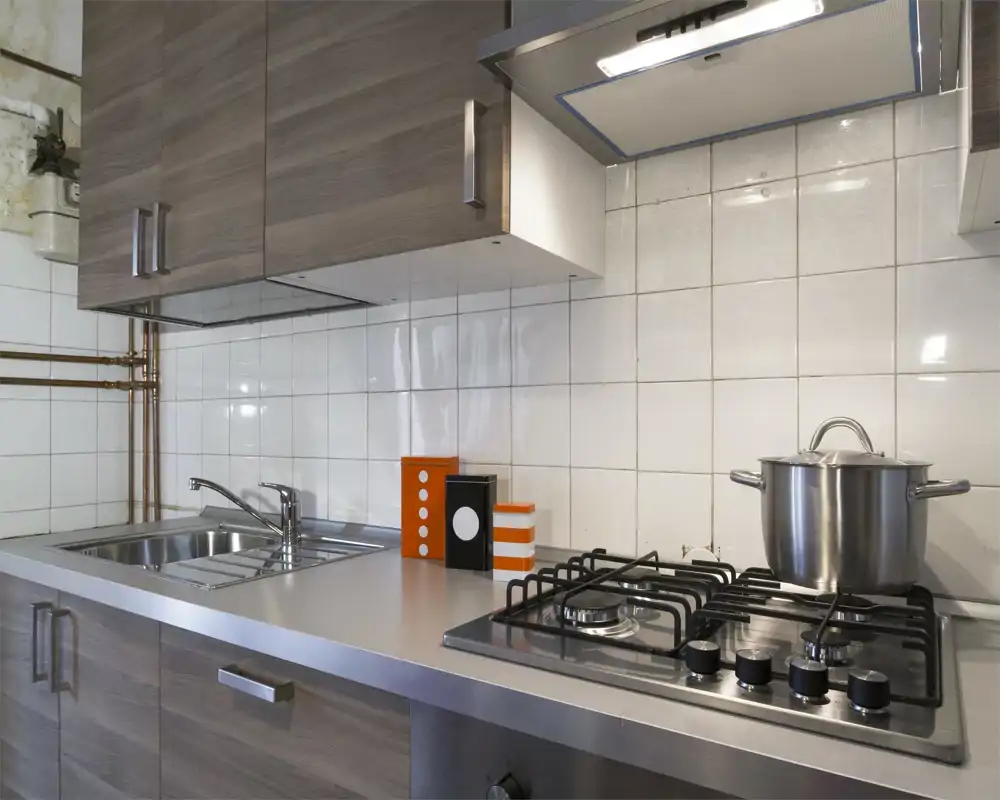Modern compact kitchen with stainless steel countertop, built-in gas hob, sink and wooden-effect cabinets. Clean, functional layout ideal for a small apartment.