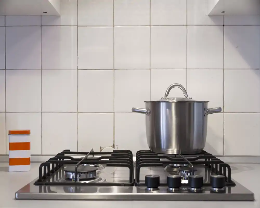 Close-up of a modern gas hob with a stainless-steel pot and tiled backsplash; clean, well-lit kitchen counter suitable for listing photos.