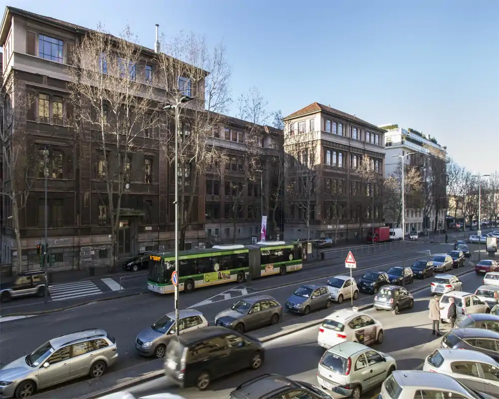 Vista sulla strada soleggiata da un balcone/finestra con edifici storici, traffico e un autobus cittadino — perfetta per mostrare la posizione e il quartiere.