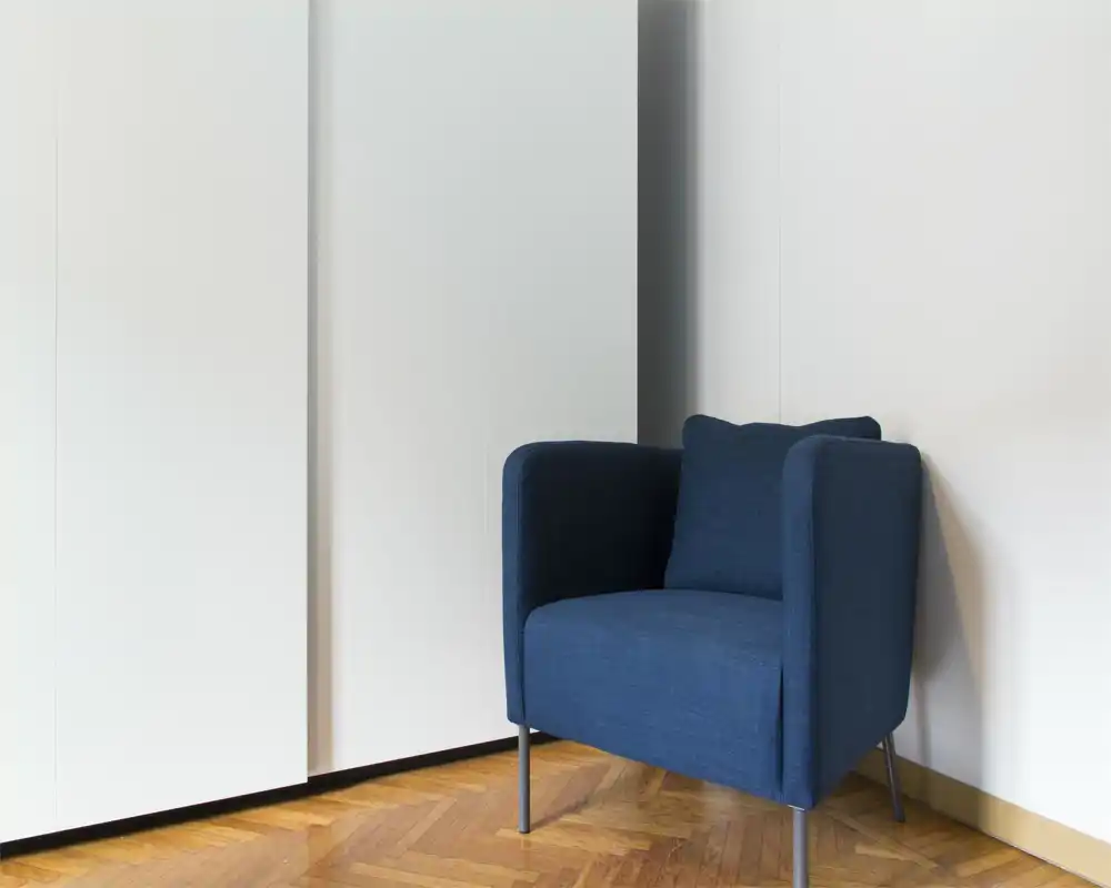 Angolo minimalista con poltrona imbottita blu scuro su pavimento in parquet; stile moderno e tranquillo, ideale come angolo lettura.
