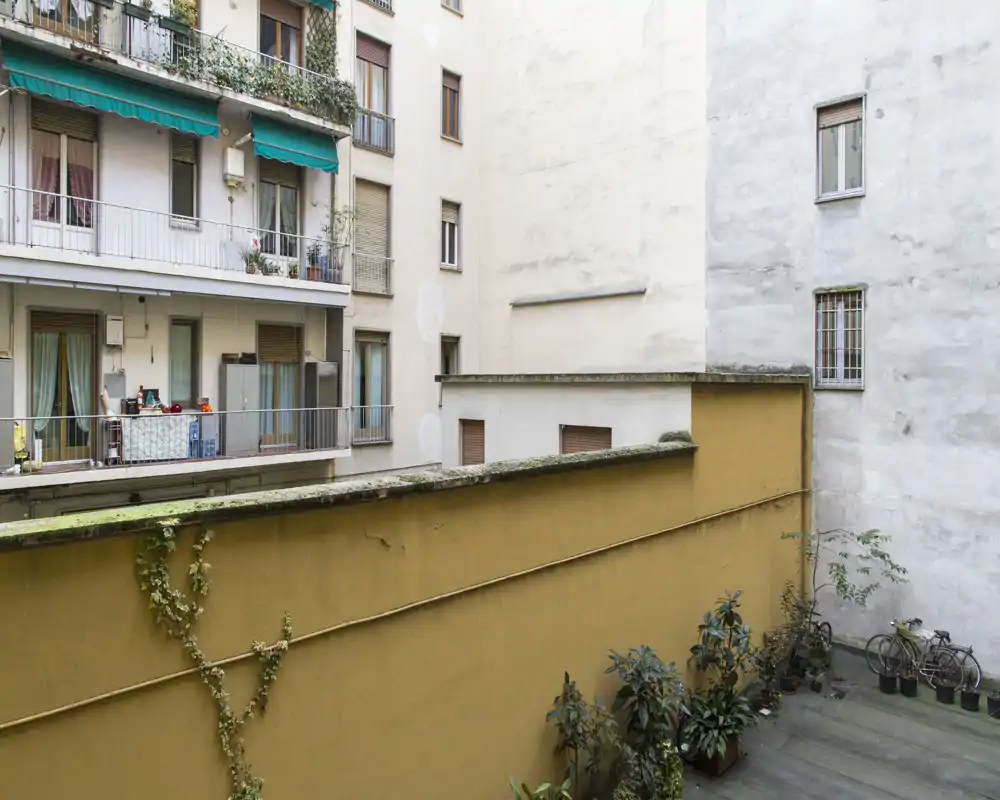 Vue sur une petite cour urbaine et les façades voisines avec des pots de plantes et un vélo ; utile pour montrer l'espace extérieur et la luminosité de l'appartement.