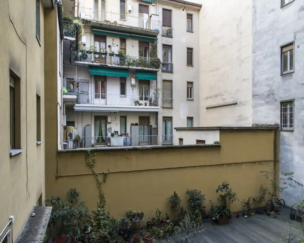 Vista di un piccolo cortile interno con balconi dei vicini, vasi di piante e pavimentazione; utile per mostrare l'area esterna/comune.