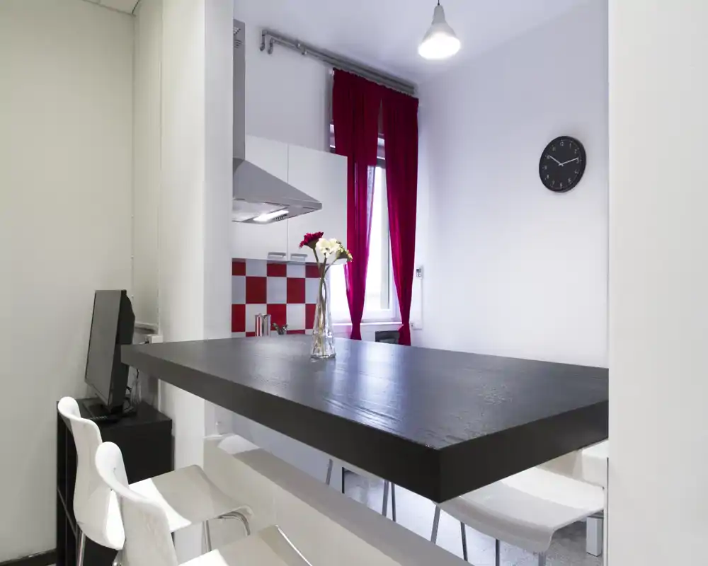 Cucina moderna con bancone, paraschizzi a quadri rossi e bianchi e tende rosse; piano in legno scuro e sgabelli bianchi per un'area colazione contemporanea.