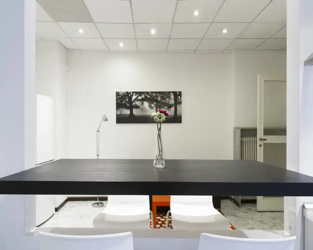 Passaggio pranzo contemporaneo con bancone alto, sedie bianche e un vaso di fiori; spazio luminoso e minimal ideale per pasti informali.