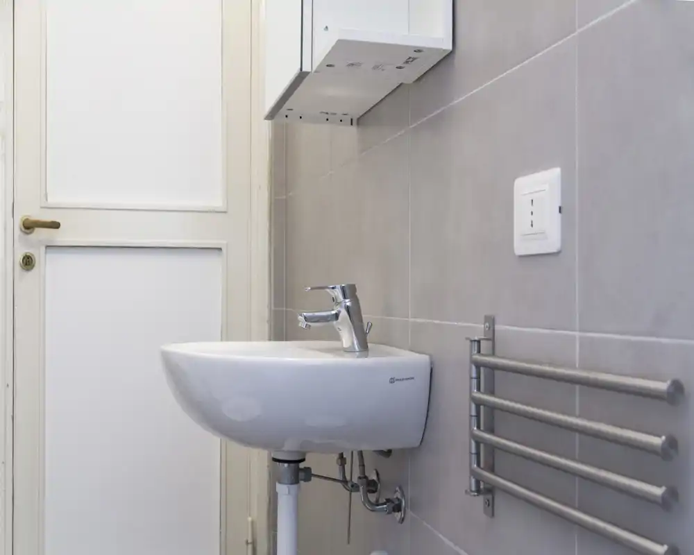 Piccolo lavabo da bagno a parete con rubinetto monocomando moderno e scalda-asciugamani su piastrelle grigie chiare.