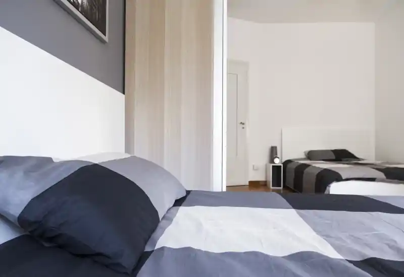 Bright, modern bedroom with twin beds dressed in coordinated grey bedding; clean lines, minimal decor and good natural light create a calm, inviting space.
