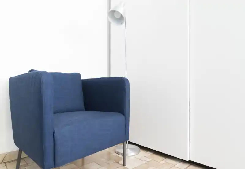 A minimal, bright corner with a modern blue armchair and a floor lamp — a calm seating spot ideal for reading or relaxing.