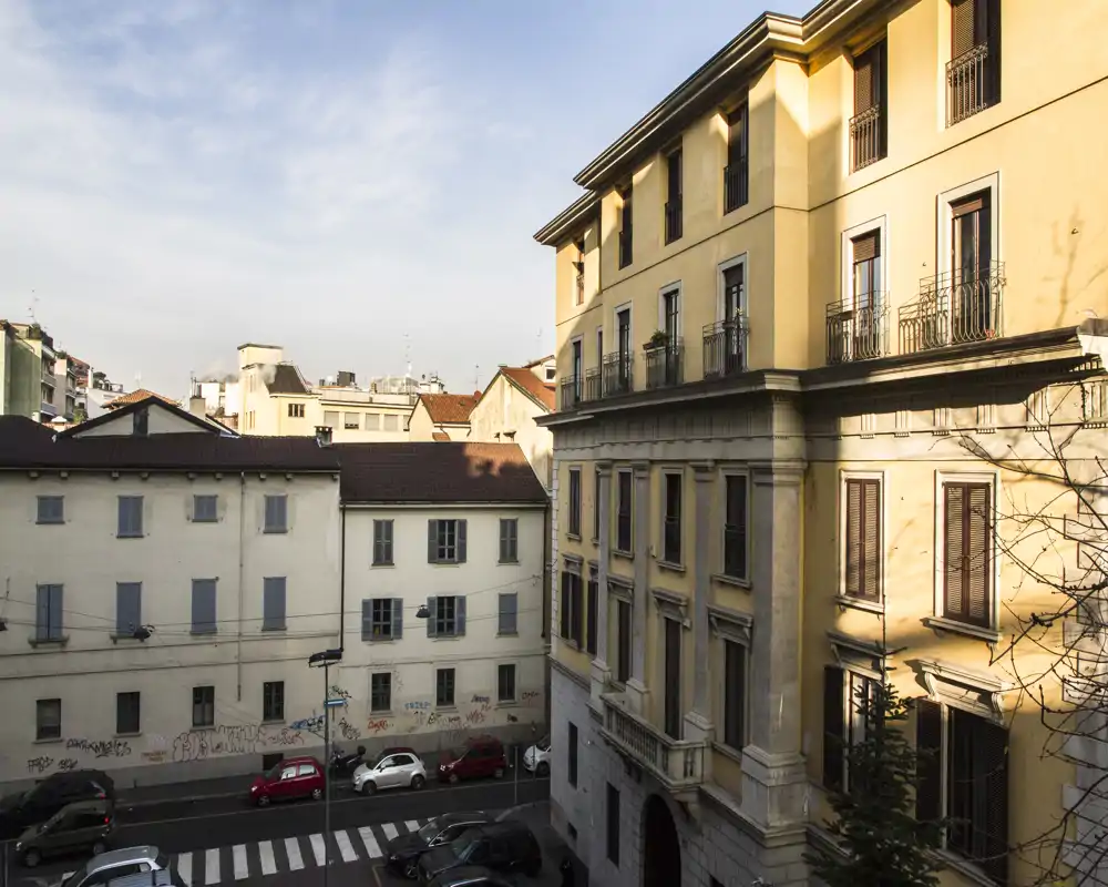 Vista exterior a la calle con edificios residenciales contiguos, balcones y coches aparcados bajo luz suave — útil para mostrar la ubicación y la fachada.