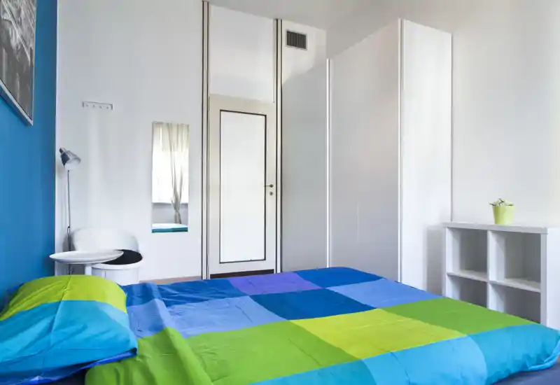 Camera da letto luminosa e moderna con letto colorato matrimoniale, armadio bianco e arredi contemporanei essenziali — perfetta per un affitto breve vivace.