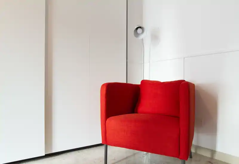 A bright, minimal corner with a bold red armchair against white walls — a simple and inviting living area accent.