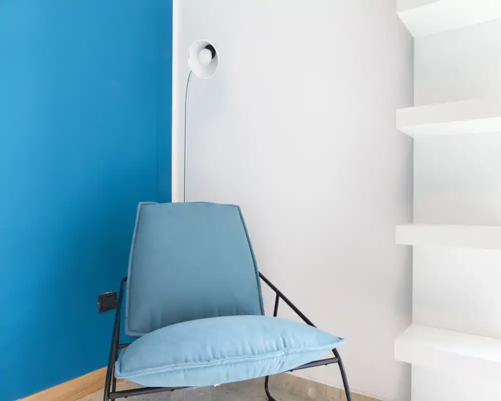 Angolo lounge minimal e moderno con una poltrona blu tenue contro una parete bicolore e una lampada da terra — un angolo rilassante ideale per leggere.