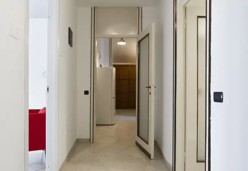 Corridoio luminoso e minimale con pareti bianche, pavimento in marmo e più porte che conducono alle stanze adiacenti. L'immagine mette in risalto lo spazio di passaggio e i dettagli d'ingresso.