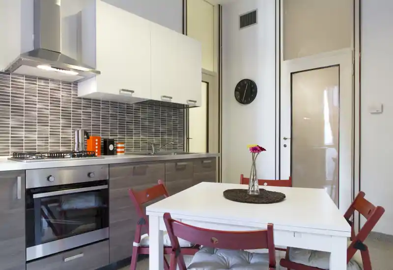 Cucina moderna a vista con forno integrato, piano cottura a gas e un piccolo tavolo da pranzo con sedie rosse; ordinata, ben illuminata e ben allestita per foto di affitti brevi.