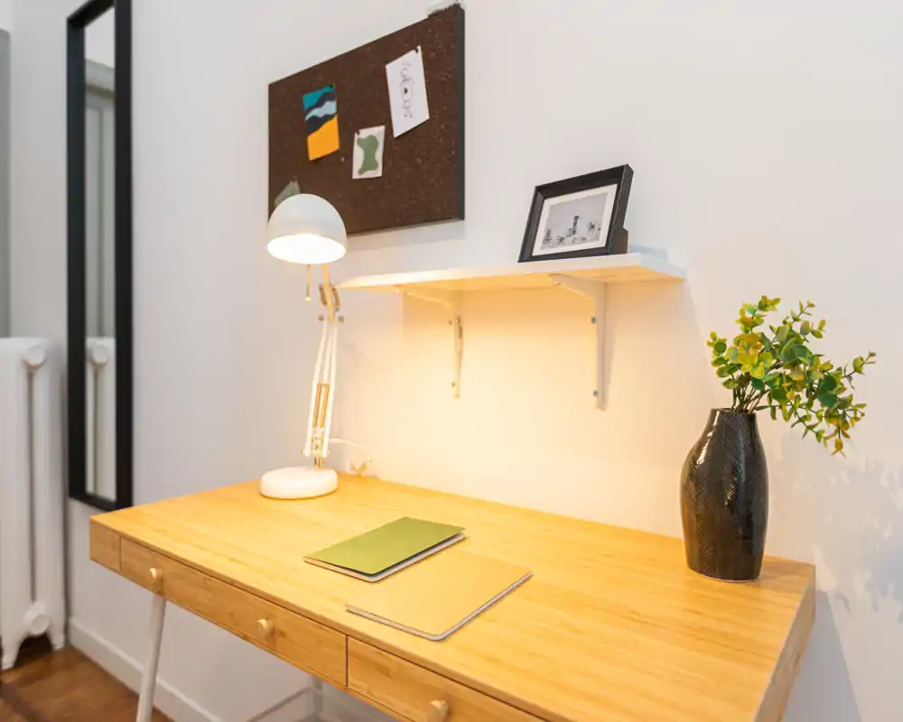 Bright, tidy workspace corner with a wooden desk, task lamp, corkboard and a decorative plant — ideal for study or remote work.