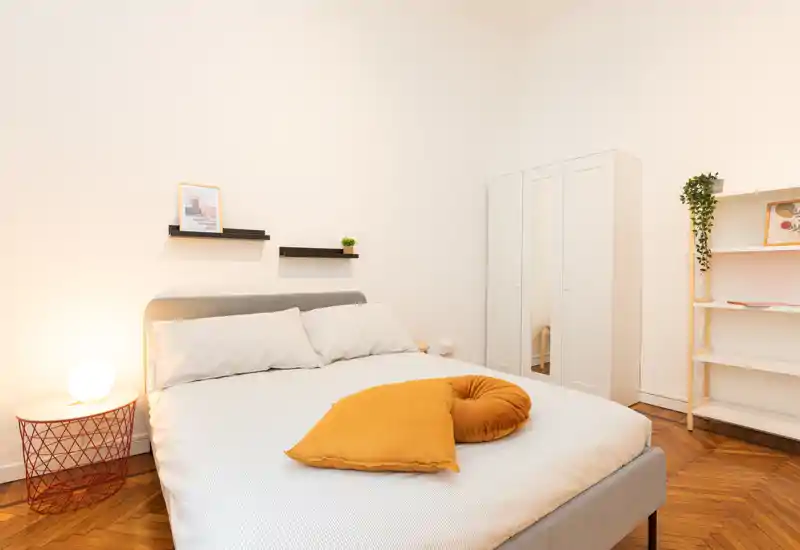 Bright, well-staged bedroom with a double bed, warm cushions and a bedside lamp; clean lines and light parquet flooring create a cozy, modern feel.