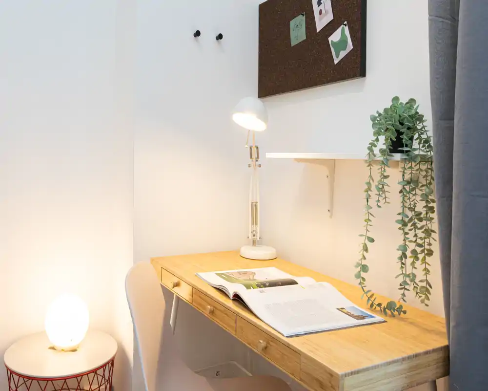 Angolo studio compatto e di design con scrivania in legno, lampada da tavolo, pianta sospesa e sedia confortevole — perfetto per leggere o lavorare da remoto.