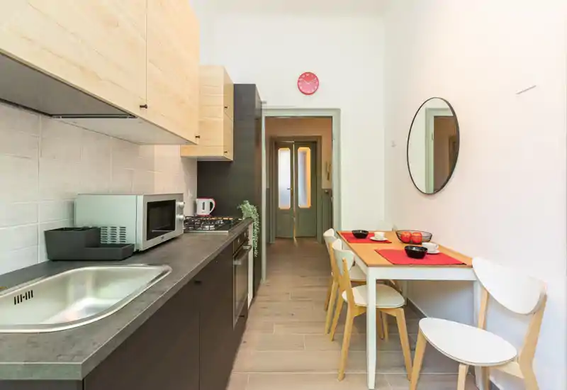 Cucina moderna a corridoio luminosa con basi scure, pensili in legno chiaro, piano cottura integrato, microonde e un piccolo tavolo da pranzo per quattro — perfetta per appartamenti urbani compatti.
