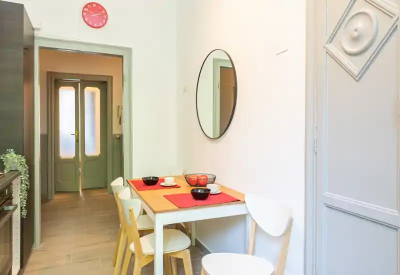 Accogliente angolo cucina con un piccolo tavolo in legno apparecchiato per due, sedie moderne e luce naturale soffusa—perfetto per colazioni informali.