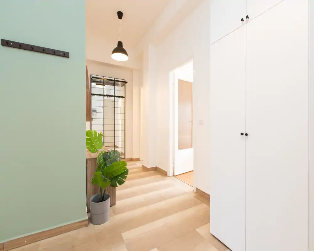 Ingresso luminoso e minimal con armadiatura a muro, lampada a sospensione e pianta decorativa; linee moderne e toni neutri creano un ambiente d'accoglienza.